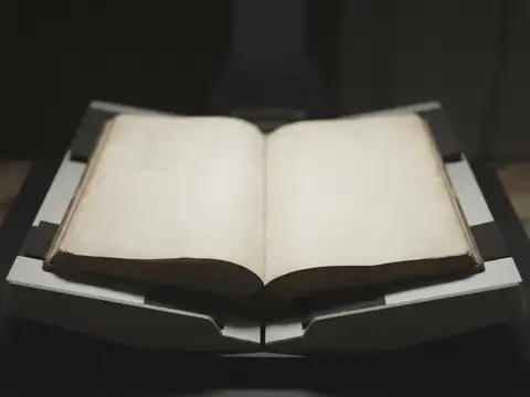Розкрита стара книга лежить у V-подібній колисці для зйомки, корінець не притиснутий